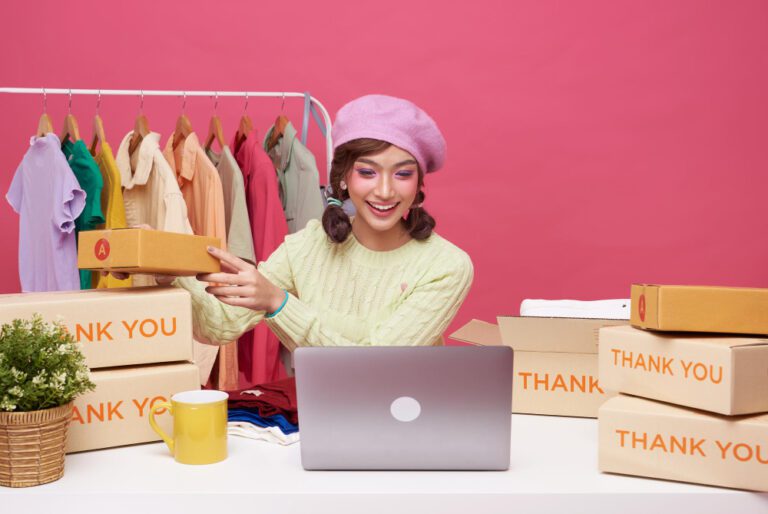 young-asian-woman-startup-small-business-freelance-sale-fashion-clothing-with-parcel-box-computer-laptop-table-sitting-isolated-pink-background-online-marketing-delivery-concept
